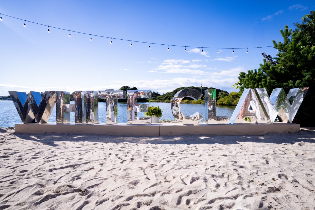 Oversized mirror-finish WHITE CLAW letters on a plinth base at the edge of Fort Pond in Montauk